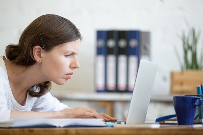 En kvinne lener seg tett inntil skjermen på en laptop mens hun myser